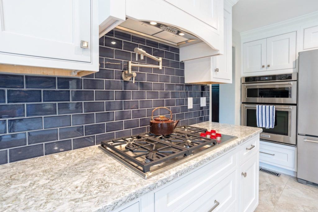 Modern kitchen with a gas stovetop, marble countertop, and dark blue subway tile backsplash.
